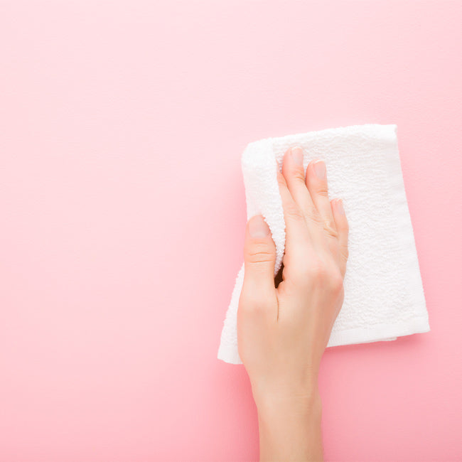 Hand, die mit einem weißen Tuch über eine Wand wischt, welche mit abwaschbarer Wandfarbe gestrichen wurde.