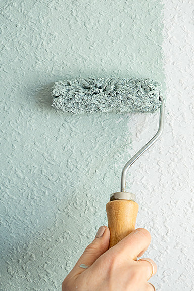 Tapete an der Wand wird mit einem Farbroller grün gestrichen
